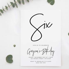 a white card with the word six on it next to eucalyptus leaves and greenery