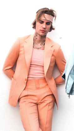 a man in an orange suit leaning against a wall with his hands on his hips