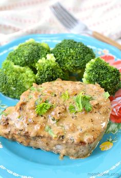 a blue plate topped with meat covered in gravy next to broccoli