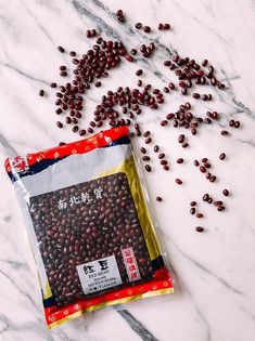 a bag of red beans sitting on top of a white marble counter next to a pile of seeds