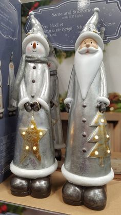 two metal santa claus figurines with lights on their feet and one holding a star