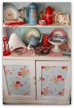 an old china cabinet with dishes and cups on it's shelves, all covered in floral fabric