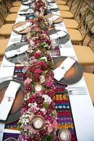 a long table is set with place settings and flowers on the runner, along with silverware