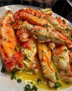 a white plate topped with pasta covered in sauce and shrimp claws on top of green garnish