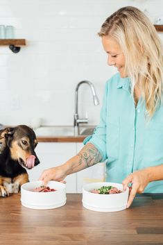 a woman and her dog are eating out of their bowls on the kitchen counter top