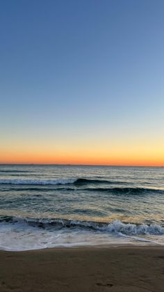 the sun is setting over the ocean with waves coming in