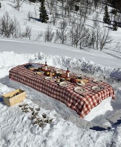 a picnic table set up in the snow with plates on it and food spread out