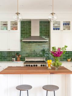 two stools sit in front of a kitchen island with flowers on it and green tile backsplash