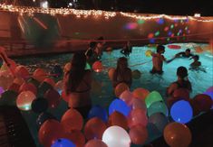 people are in the pool with balloons and streamers floating around them at night time