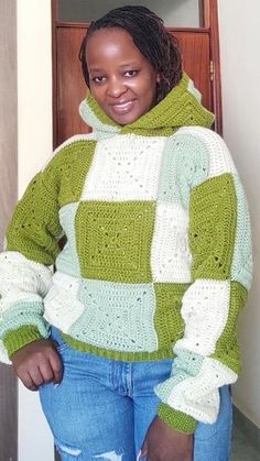 a woman standing in front of a door wearing a green and white crocheted sweater