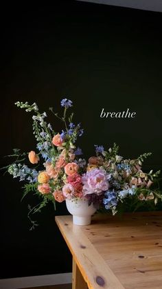 a vase filled with flowers sitting on top of a wooden table next to a black wall