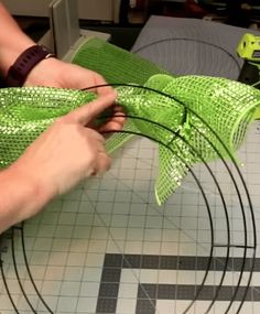 a person is making a green bow out of sequins on a table top