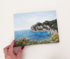 a hand holding up a painting of the ocean