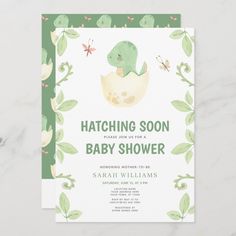 a green and white baby shower card with a dinosaur in an egg on it's back