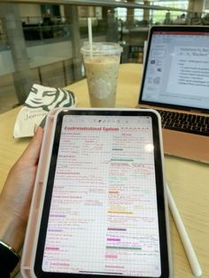 a person holding an electronic device in front of a laptop computer on a table with a cup of coffee