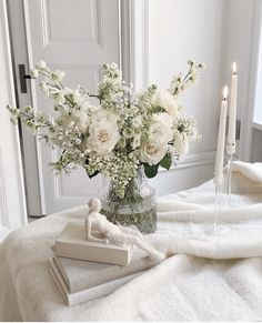 a vase filled with white flowers sitting on top of a bed next to two candles