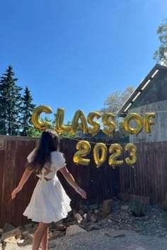 a woman in a white dress standing next to a fence with the words class of 2093 on it