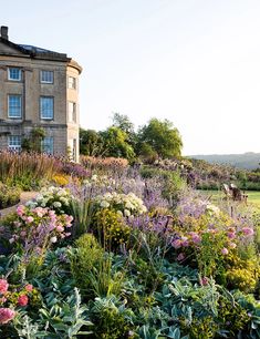 a large garden with lots of flowers in front of a big house on a hill