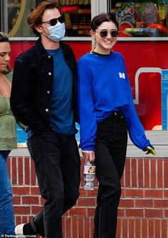 a man and woman walking down the street wearing face masks