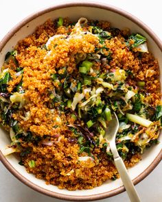 a bowl filled with rice and vegetables on top of a white tablecloth next to a spoon