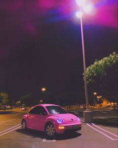 a pink car is parked in a parking lot at night with the lights turned on