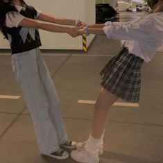 two young women are holding hands in an empty parking lot, one is wearing a skirt and the other has a tie