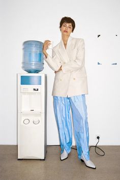 a woman standing next to a water dispenser in front of a white wall