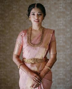 a woman in a pink sari with gold jewelry on her neck and hands behind her back