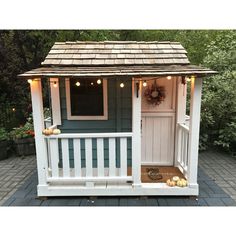 a small white shed with lights on the front door and side porch, along with pumpkins