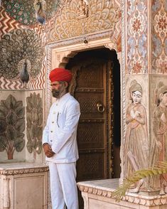 a man in a turban standing by a door with paintings on the walls