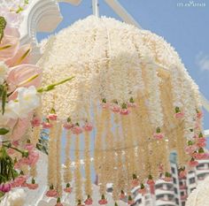 an umbrella with flowers hanging from it in front of a building that has white and pink decorations