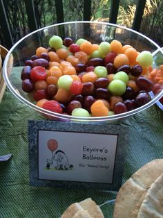 a bowl full of grapes and oranges on a table with other foods in the background