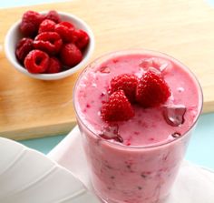 raspberry yogurt smoothie in a glass next to a bowl of raspberries