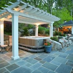 an outdoor hot tub surrounded by stone walls and pergolated patio area with seating