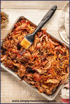 a pan filled with shredded meat next to a spatula on top of a wooden table