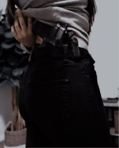 a woman in black jeans and a gray shirt holding a cell phone up to her waist