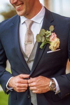 a man wearing a suit and tie with a flower in his lapel is smiling