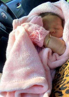 a baby wrapped in a pink blanket sleeping on top of a leopard print car seat