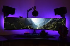 a computer desk with two monitors and headphones on it in front of a purple light