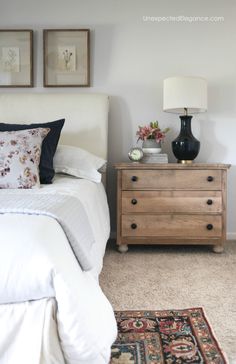 a white bed sitting next to a wooden dresser with two lamps on top of it