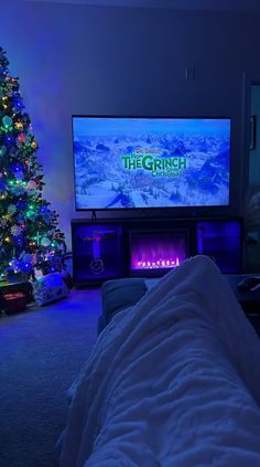 a living room with a christmas tree in the corner and a large television on top of it