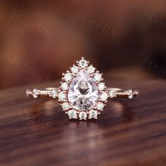 an engagement ring with a pear shaped diamond surrounded by smaller round diamonds on a wooden surface