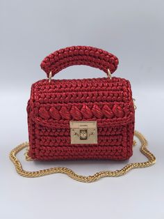 a red crocheted purse with a gold chain hanging from the front, on a white background