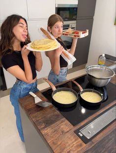 two young women are making pancakes on the stove top and one is holding a plate