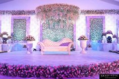 a stage set up for a wedding ceremony with flowers and greenery on the walls