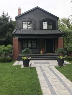 a black house with two large planters on the front lawn and steps leading up to it