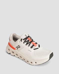 a white sneaker with an orange and black lace on the side, in front of a