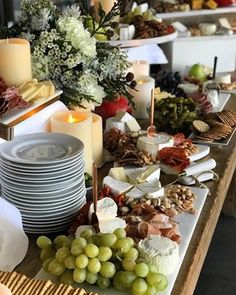 a table topped with lots of food and plates covered in cheese, crackers and grapes