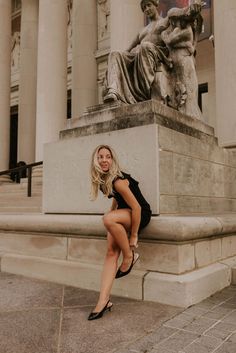 a woman is sitting on a bench in front of a building with columns and statues