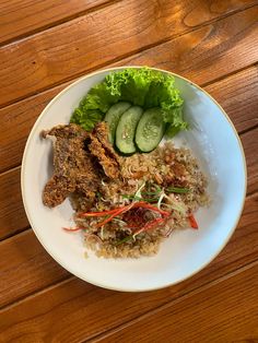 a white plate topped with rice and meat next to cucumbers on top of a wooden table